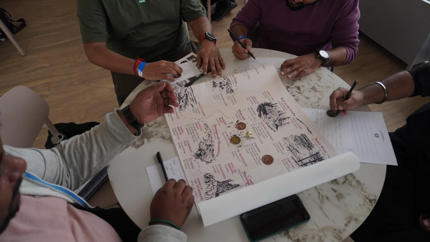Overhead view of four players writing on a large printed region map spread across a round table