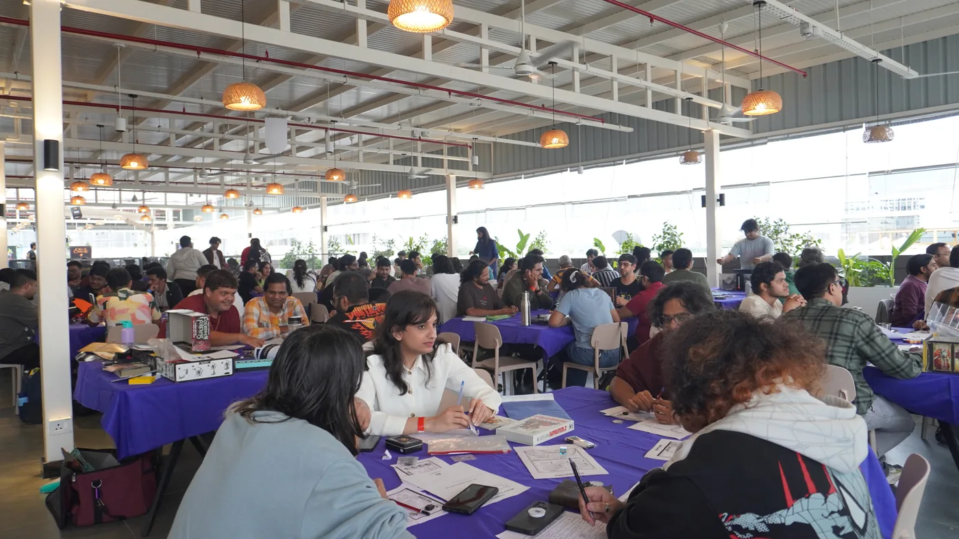 Wide daylight view down a long hall packed with players at purple tables under industrial ceiling lights
